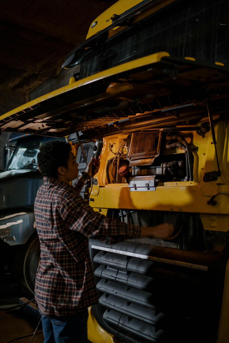 Fleet technician working under the raised hood of a heavy truck