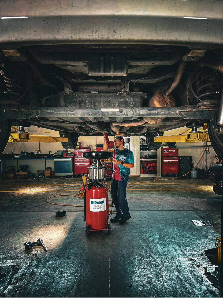 Utility fleet maintenance technician working under a vehicle in an industrial shop